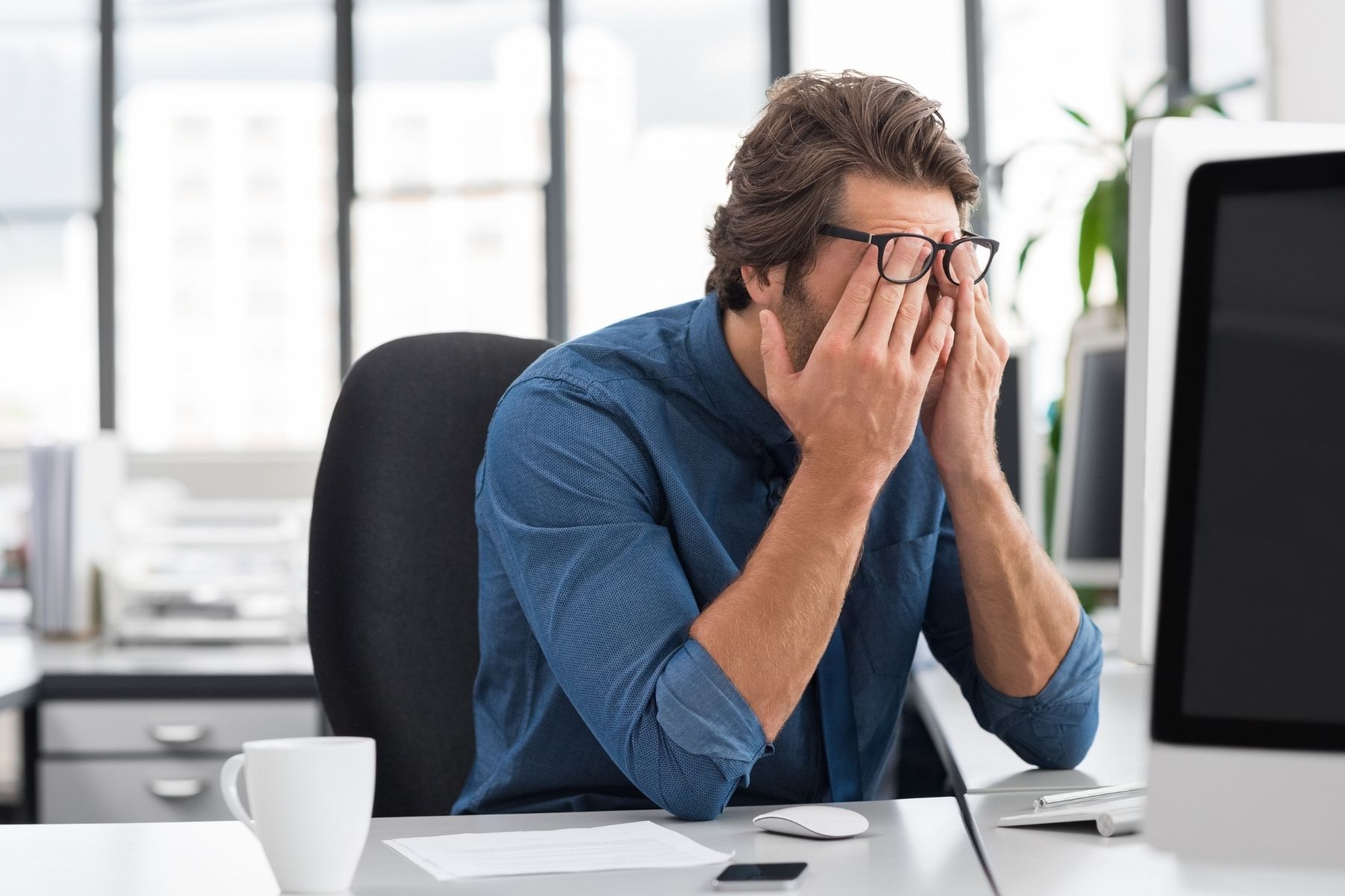 A man with glasses rubbing his face in his office